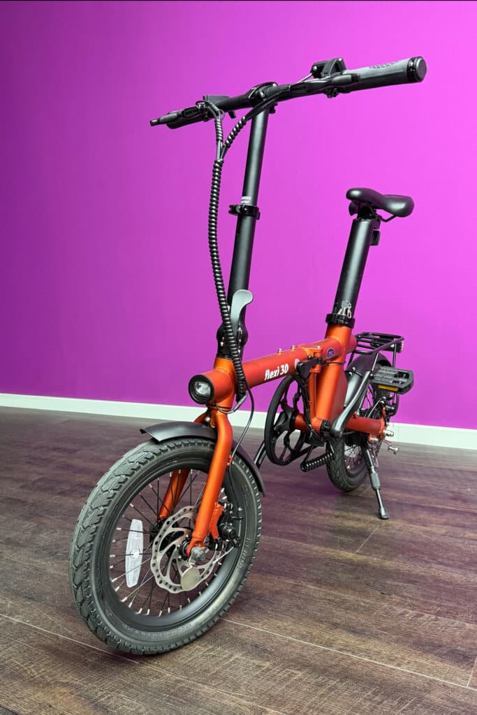 Faltbares orangefarbenes E-Bike vor lila Wand